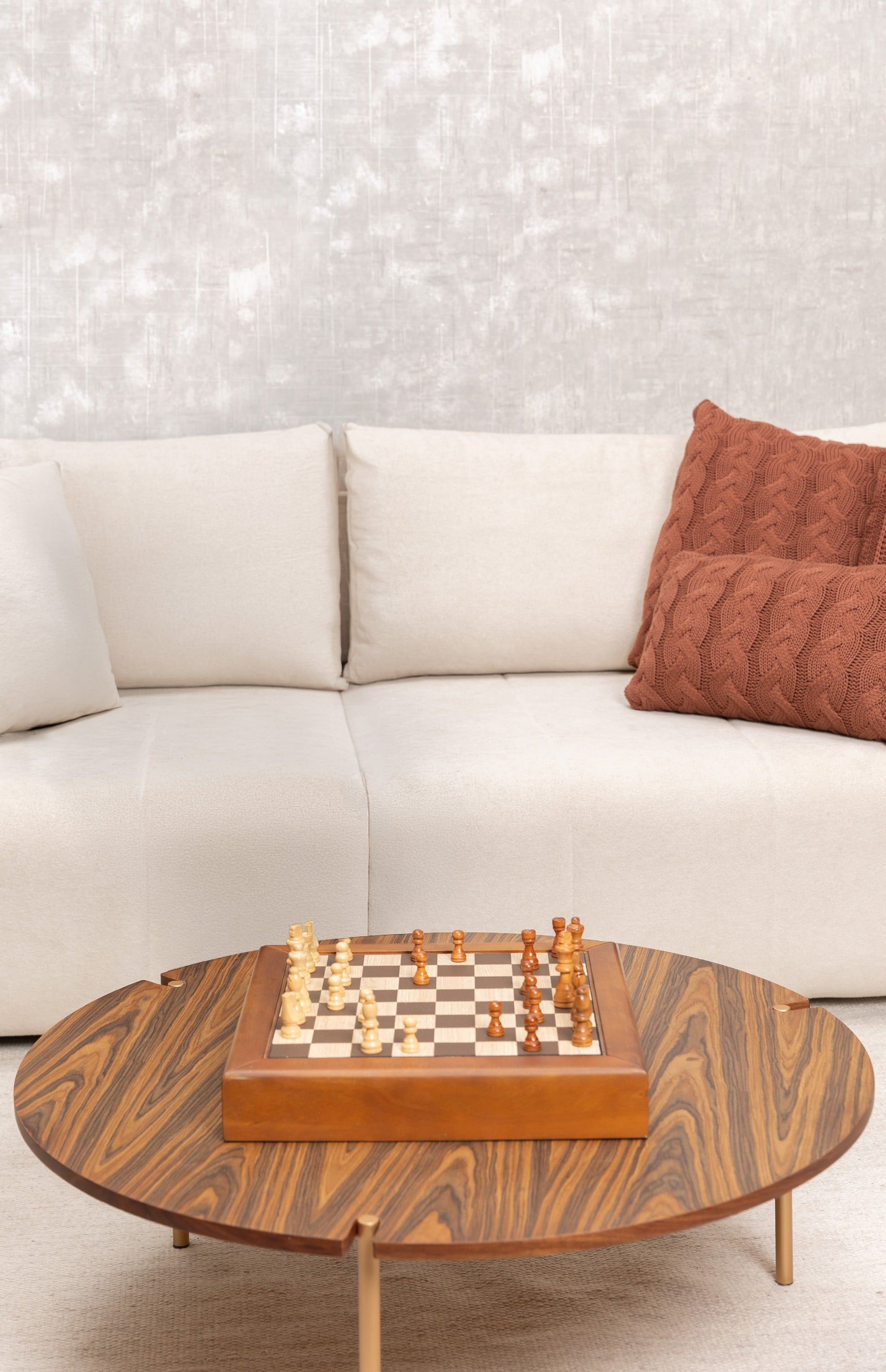 Sala com sofá creme, almofadas terracota e um tabuleiro de xadrez sobre a mesa