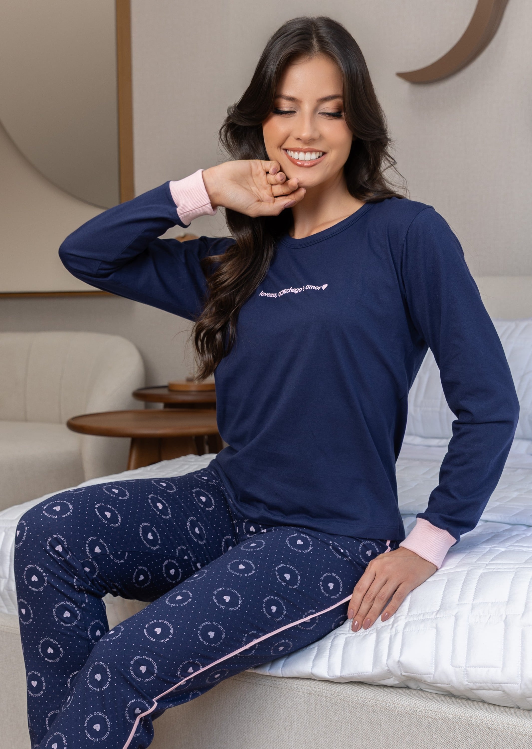 Mulher de pijama azul-marinho com punhos rosa sentada na cama